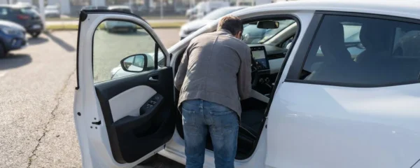 Acheteur vu de dos inspectant le tableau de bord et l'écran tactile d'une Renault Clio 5 d'occasion sur un parking de concession